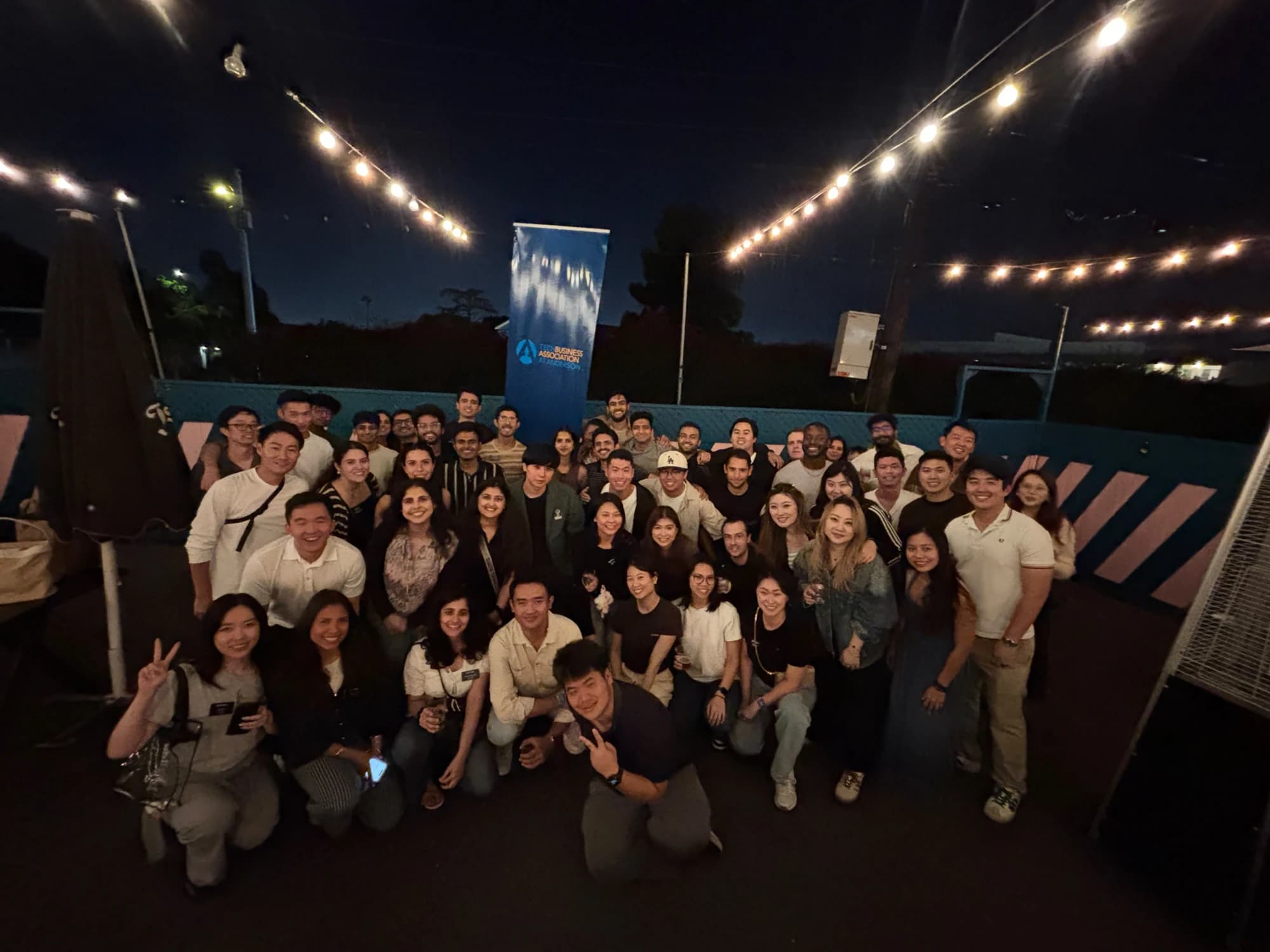 A large group of AnderTech members and guests posing together at an evening mixer under string lights